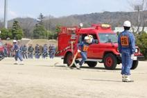 消防車の前を放水ホースを持って走る隊員の写真