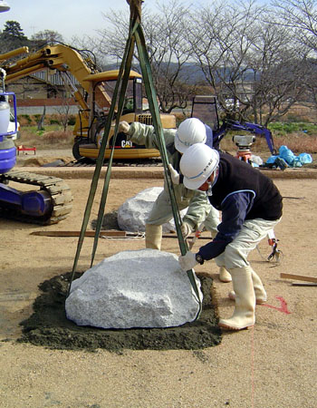 大きな石を設置する二人の男性の写真
