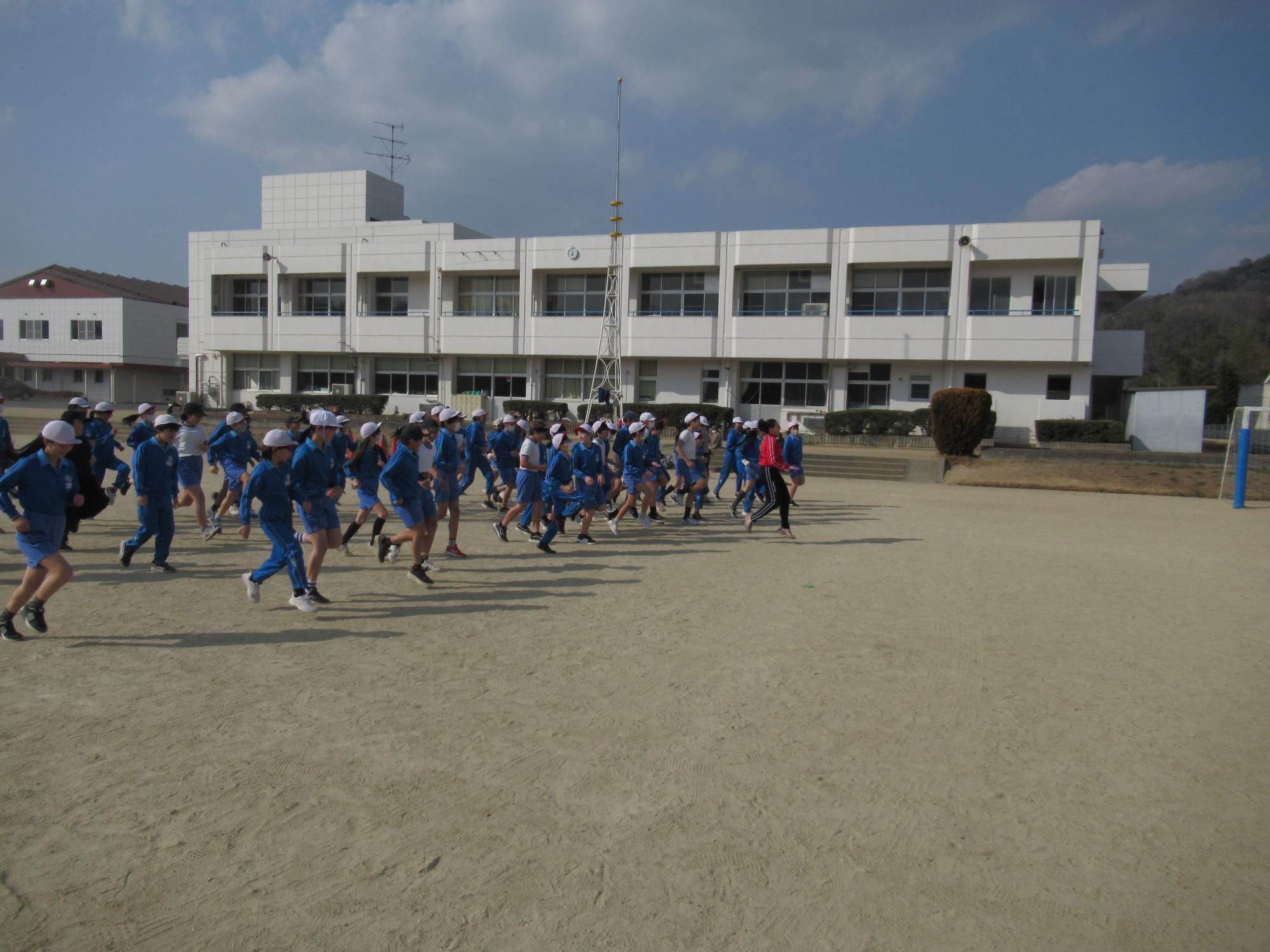 小学生と運動場を走りながらウォーミングアップをするカナダのコーチ