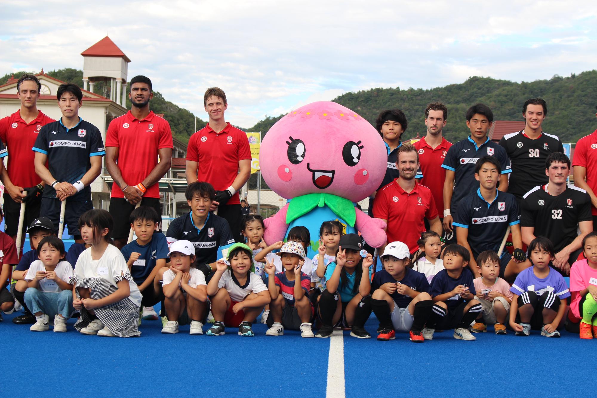 親善試合前の日本代表チーム、カナダ代表チーム、あかいわモモちゃんとエスコートキッズのみなさん